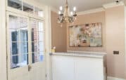 A small reception area with a white desk, abstract painting on the wall, chandelier, and glass-paned door leading outside.