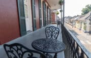 Ornate black metal table and chairs on a balcony with red walls, overlooking a street lined with historic buildings and hanging plants.