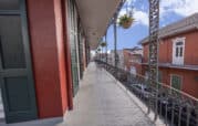Balcony view of a New Orleans street, with ornate iron railings, hanging plants, and colorful buildings.