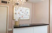 A room with a chandelier, a framed abstract painting of birds, a black countertop, and a gold tissue box against light pink walls.