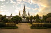 Jackson Square in New Orleans features a bronze equestrian statue of Andrew Jackson, surrounded by trees and plants, with St. Louis Cathedral and a partly cloudy sky in the background.